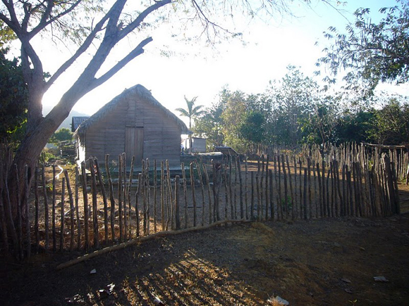 Una casa humilde, sacada de un dibujo infantil: techo de guano, cerca de maderas en fila y un panel solar. Foto: Josué Labaut