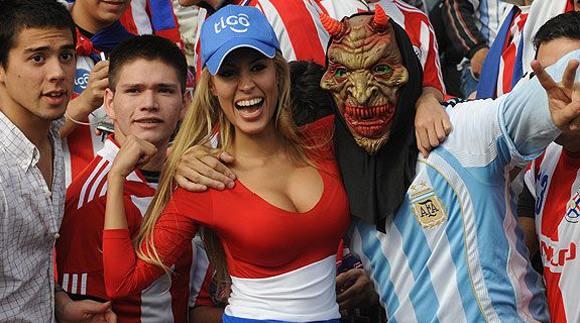 Una fanática de Paraguay alienta a su equipo junto a un simpatizante de la selección argentina en las tribunas del estadio cordobés