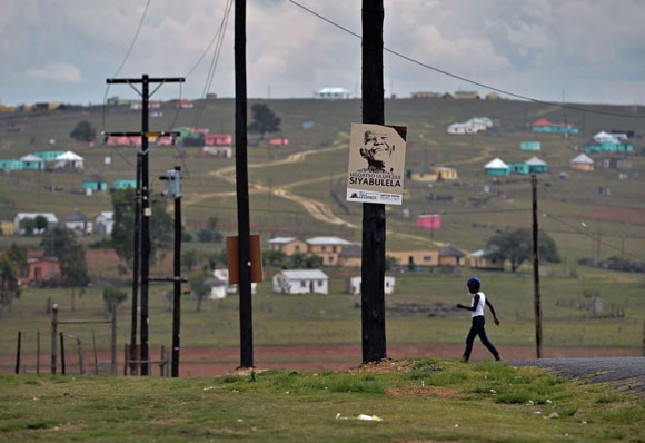 Un niño camina junto a un cartel con la imagen de Nelson Mandela en Qunu (Sudáfrica), cerca de la granja donde el líder sudafricano paso su infancia. Foto: CARL DE SOUZA (AFP)