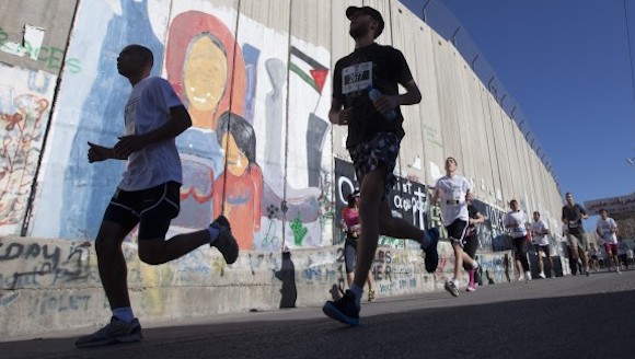 Palestinos y extranjeros, incluyendo activistas por la paz, corriendo en la ruta a lo largo del Muro de Separación en el Segundo Maratón Internacional Palestino, en la ciudad de Belén. Participaron unos mil corredores. israel prohibió el acceso de unos 30 participantes, incluyendo un atleta olímpico. AP Photo/Majdi Mohammed