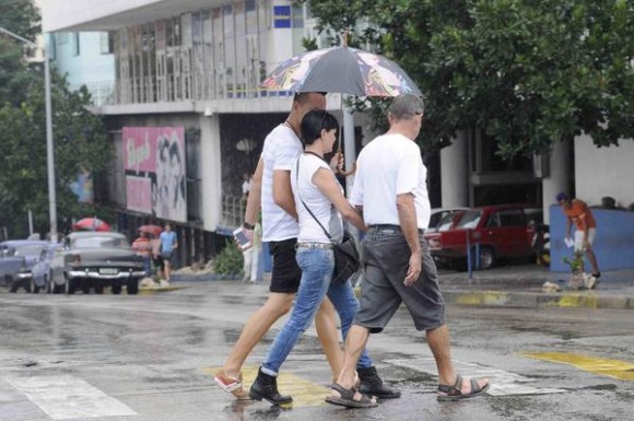 Personas protegiéndose de la lluvia mientras cruzan por la esquina de las calles 23 y L, en El Vedado