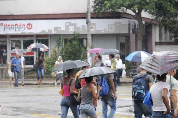 Personas protegiéndose de la lluvia mientras cruzan  por la esquina de las calles 23 y L