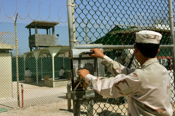 Un guardia se abre una puerta, mientras que en el fondo dos detenidos se sientan en un área de descanso detrás de esgrima, en el recinto del Campo Delta 4 prisión administrada militar, en la Base Naval de la Bahía de Guantánamo Estados Unidos, Cuba 27 de junio 2006. Foto: Brennan Linsley/ Reuters.