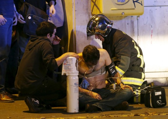 French fire brigade members aid an injured individual near the Bataclan concert hall following fatal shootings in Paris, France