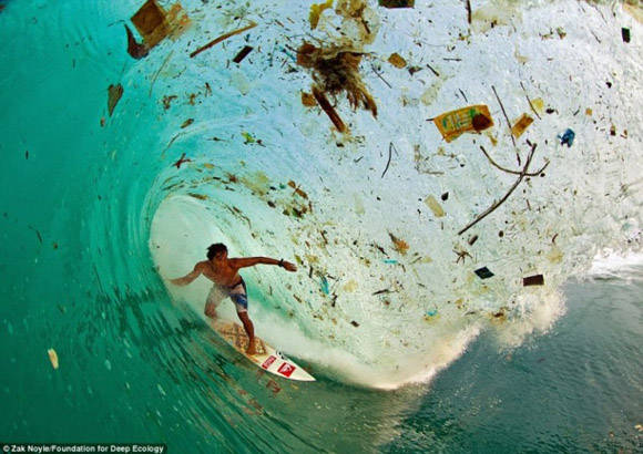 La persona que practica surf de Indonesia Dede Surinaya cabalga una ola de suciedad y basura (Java, Indonesia).