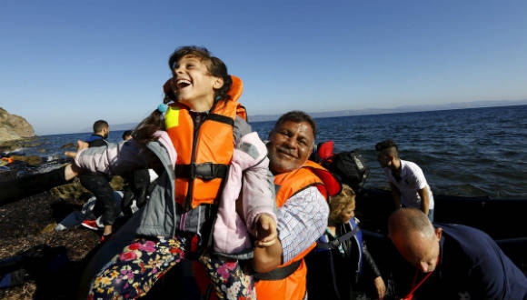 Una niña refugiada sonríe en brazos de su padre poco después de llegar en lancha a la isla griega de Lesbos tras cruzar una parte del mar Egeo desde Turquía el 18 de septiembre de 2015. Foto: Reuters