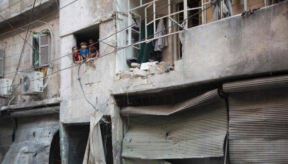 Niños sirios se asoman por la ventana de un edificio derrumbado por los bombardeos en Alepo. Foto: AFP.