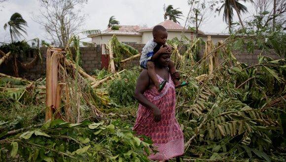 Una mujer lleva un niño caminando entre los árboles talados por el huracán Mateo en Les Cayes, Haití. Foto: Reuters. 
