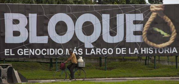 A man carries a gas cylinder on the back of his bicycle as he passes a billboard that reads in Spanish "Blockade: The longest genocide in History" in Havana, Cuba, Tuesday, Jan. 26, 2016. The Obama administration is loosening the U.S. trade embargo on Cuba with a new round of regulations allowing American companies to sell to Cuba on credit and export a limited number of products to the Cuban government, officials said Tuesday. (AP Photo/Desmond Boylan)