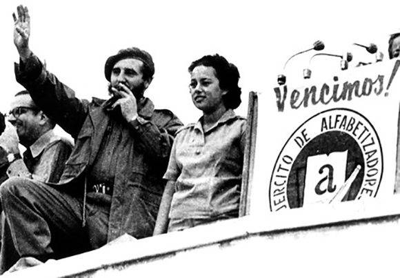 Fidel saluda a los alfabetizadores en la concentración en la Plaza de la Revolución "José Martí", para proclamar a Cuba Territorio Libre de Analfabetismo, lo acompaña una joven alfabetizadora, el 22 de diciembre de 1961. Fuente: Periódico Escambray / Sitio Fidel Soldado de las Ideas.