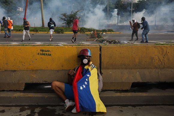 Un manifestante de la derecha venezolana se esconde mientras sus compañeros lanzan explosivos.  Foto: EFE.