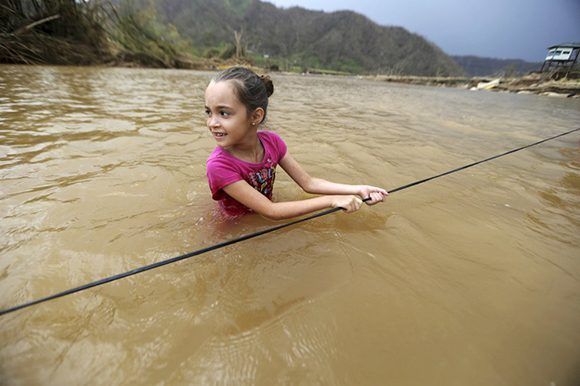 Una niña cruza un río agarrándose a una cuerda en Morovis (Puerto Rico) tras el paso del huracán. Foto: AP.